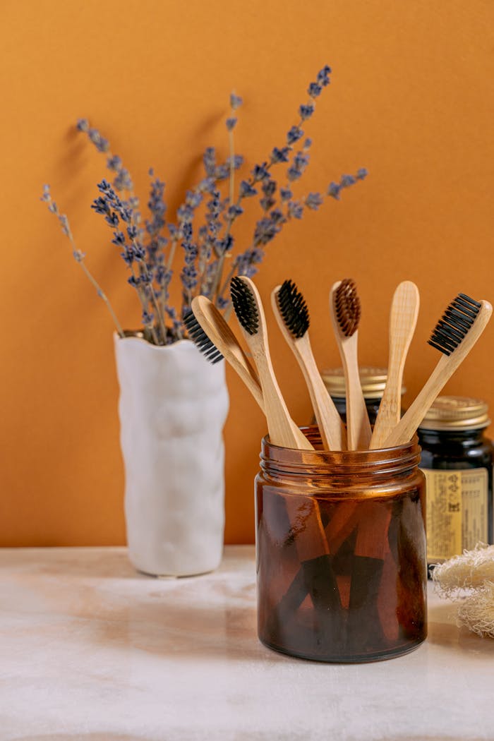 Aesthetic arrangement of bamboo toothbrushes in a glass jar alongside dried lavender decor on a marble surface.